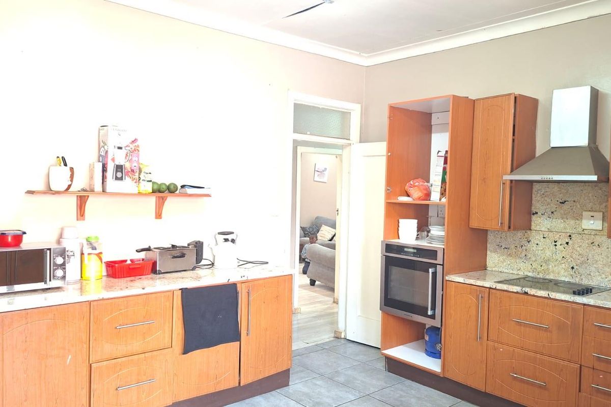 A functional kitchen featuring wood-finish cabinetry, granite countertops, built-in oven, and extractor fan, with tiled flooring and direct access to the living area.
