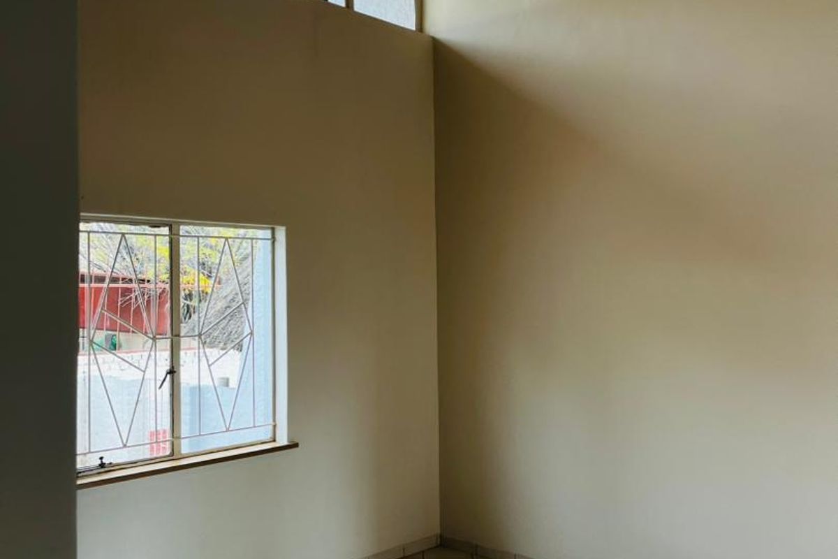 An empty living area featuring high timber-clad ceilings, clerestory windows for natural light, and neutral tiled flooring.
