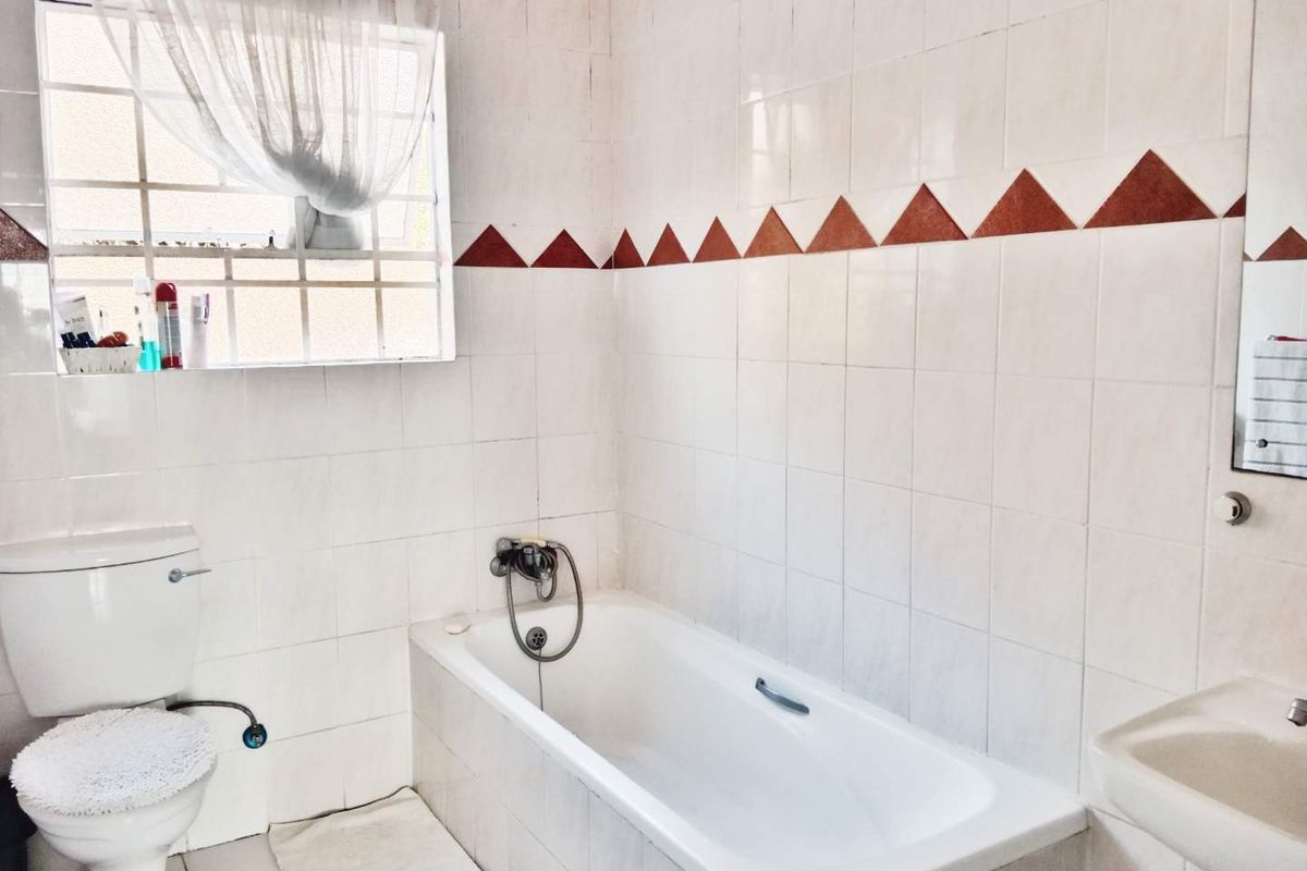 A functional bathroom featuring a standard bathtub, toilet, and wall-mounted basin with dated white wall tiles and decorative border accents.