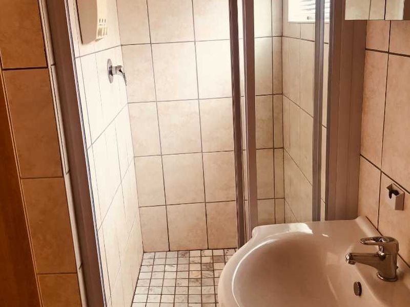 A functional bathroom featuring a tiled shower enclosure with a rainfall shower head and a pedestal basin with a mixer tap.