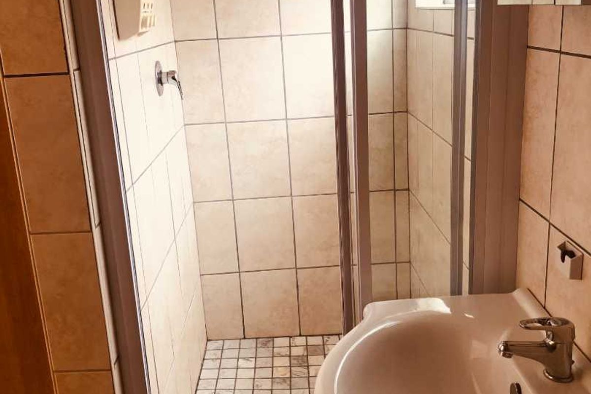 A functional bathroom featuring a tiled shower enclosure with a rainfall shower head and a pedestal basin with a mixer tap.