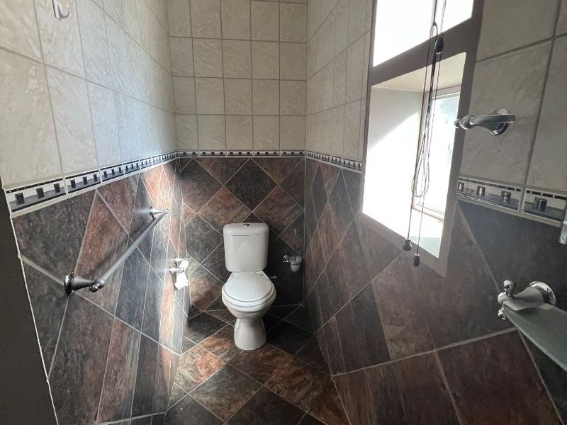A compact bathroom featuring a pedestal basin, toilet, and decorative tiled walls and flooring with natural light from a side window.