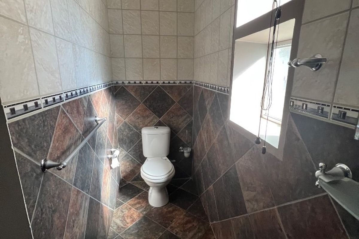 A compact bathroom featuring a pedestal basin, toilet, and decorative tiled walls and flooring with natural light from a side window.