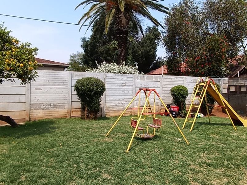 A spacious backyard garden featuring a well-maintained lawn, a paved patio area, and a secure precast concrete boundary wall.