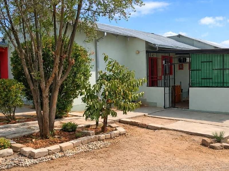 Rear view of a single-story house featuring a concrete patio, security gates, and established garden beds with stone edging.