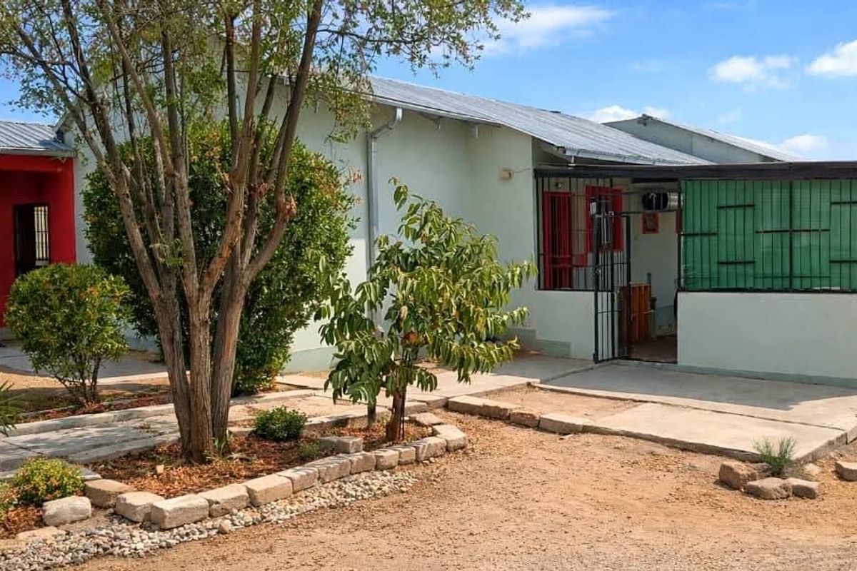 Rear view of a single-story house featuring a concrete patio, security gates, and established garden beds with stone edging.