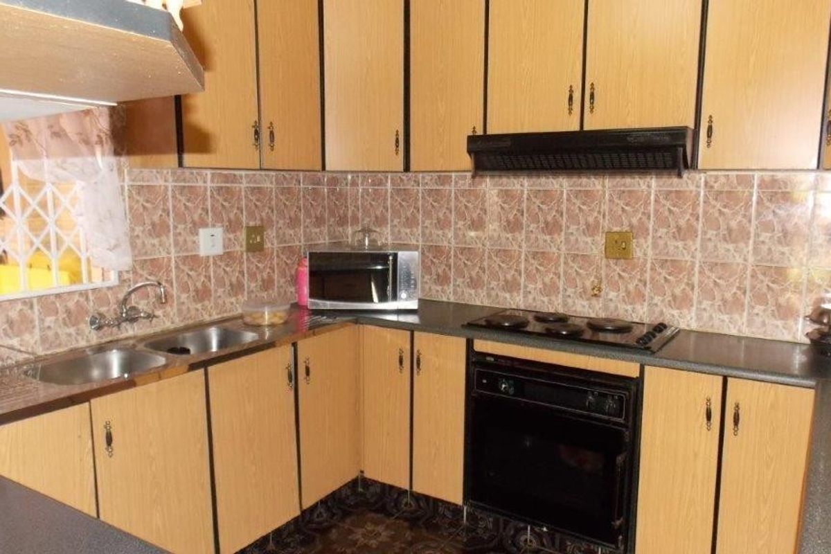 A functional kitchen featuring laminate cabinetry, dark countertops, built-in oven, electric hob, and tiled splashbacks, offering a dated aesthetic ready for modernization.