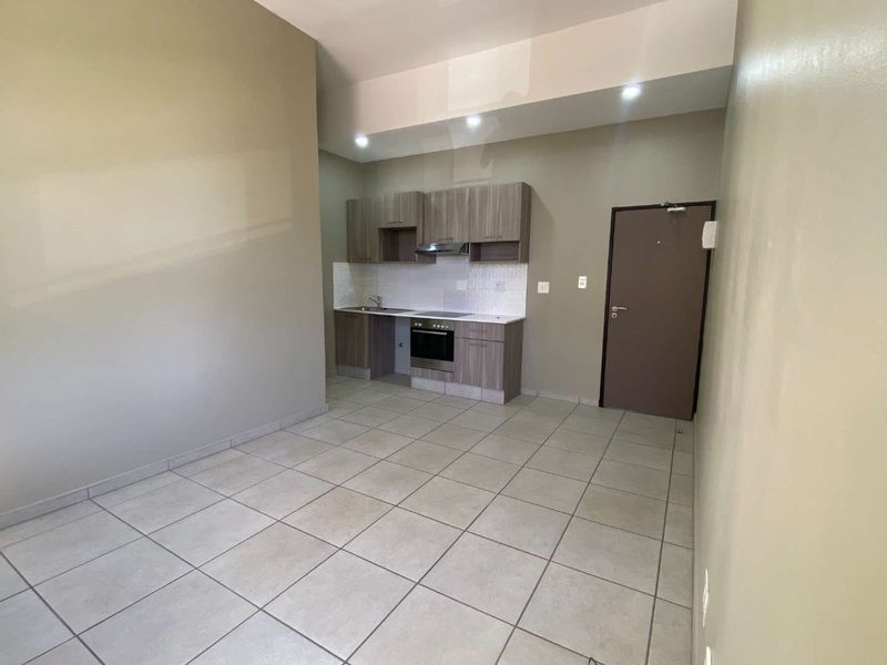 An open-plan living and kitchen area featuring modern cabinetry, built-in appliances, tiled flooring, and neutral wall tones.