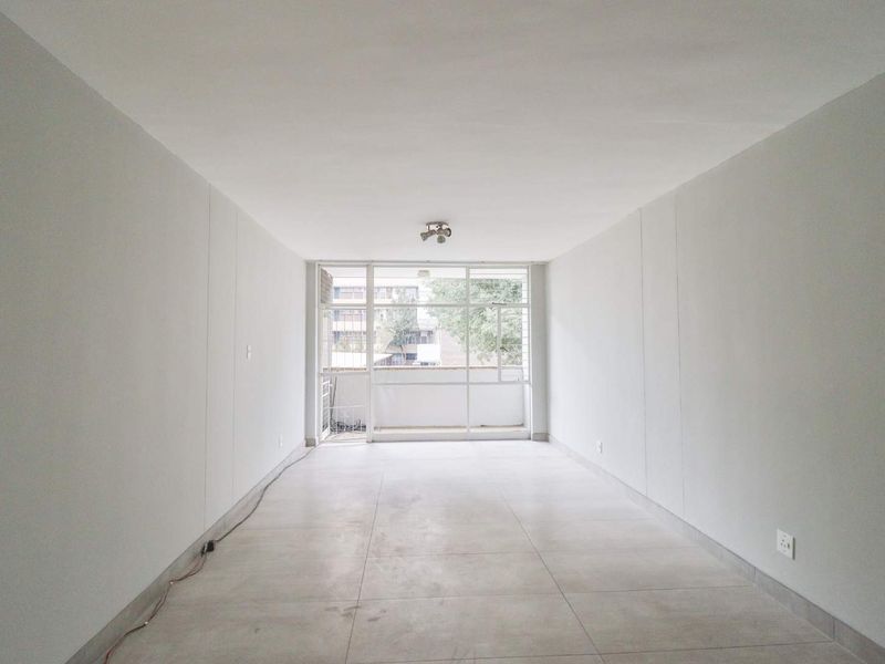A bright, empty living room featuring neutral tiled flooring and a large glass sliding door leading to an outdoor area.