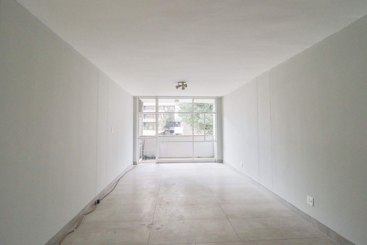 A bright, empty living room featuring neutral tiled flooring and a large glass sliding door leading to an outdoor area.
