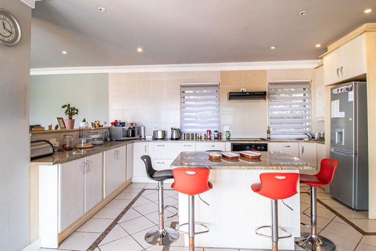 Spacious kitchen featuring granite countertops, a central island with breakfast bar seating, tiled flooring, and built-in cabinetry with integrated extractor fan.