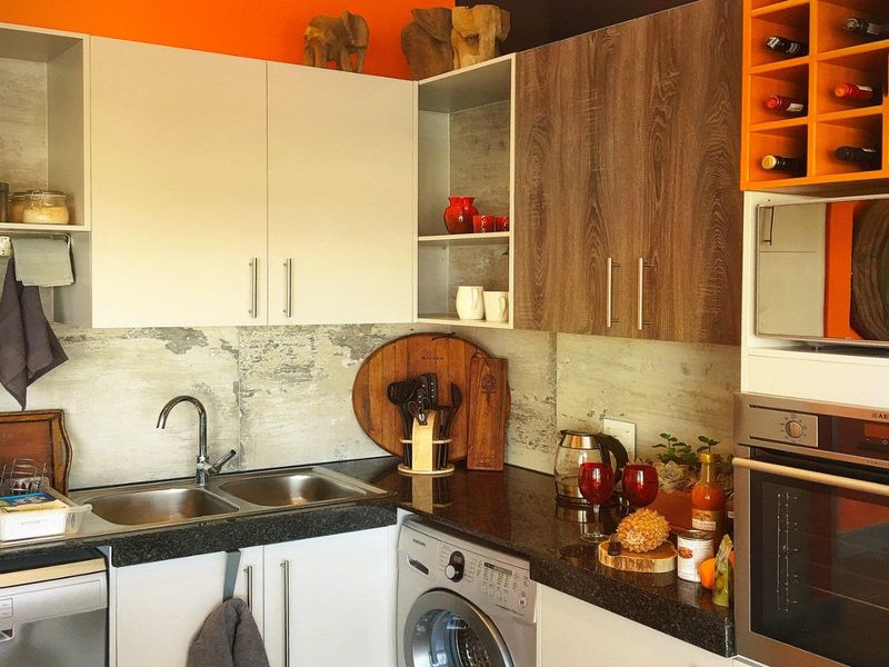 Compact modern kitchen featuring granite countertops, double stainless steel sink, built-in oven, microwave, and integrated wine storage with contemporary cabinetry.