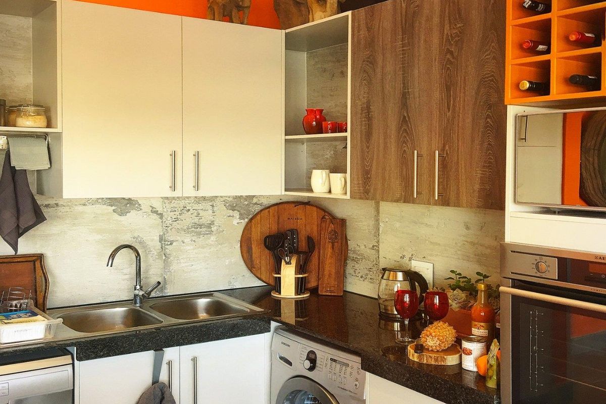 Compact modern kitchen featuring granite countertops, double stainless steel sink, built-in oven, microwave, and integrated wine storage with contemporary cabinetry.