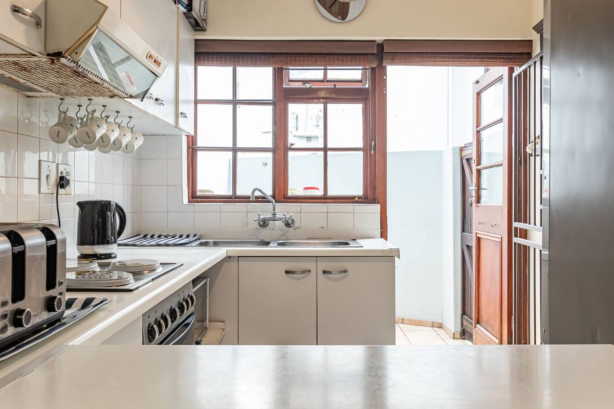 A functional kitchen featuring built-in cabinetry, an electric hob, oven, and extractor fan, with direct access to an outdoor area through a timber door.
