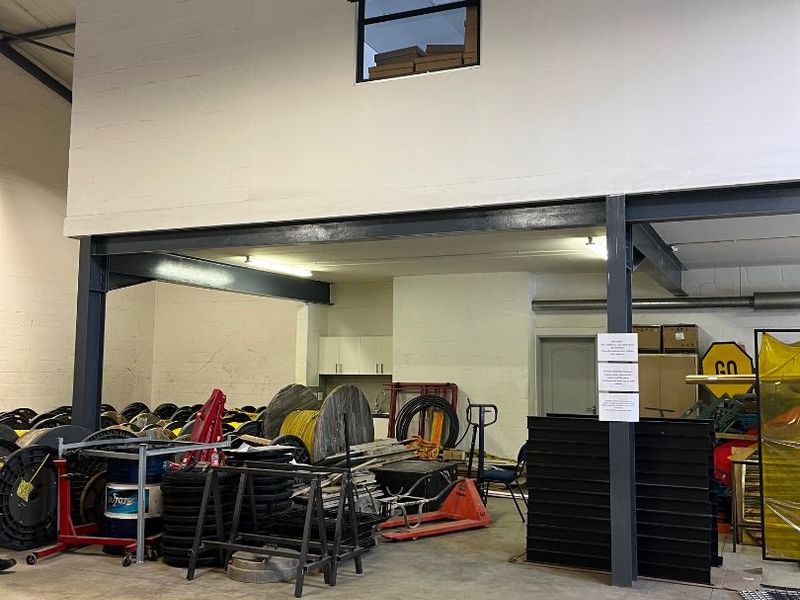 Industrial warehouse space featuring a steel mezzanine level, concrete flooring, and high-bay lighting, suitable for storage or workshop operations.
