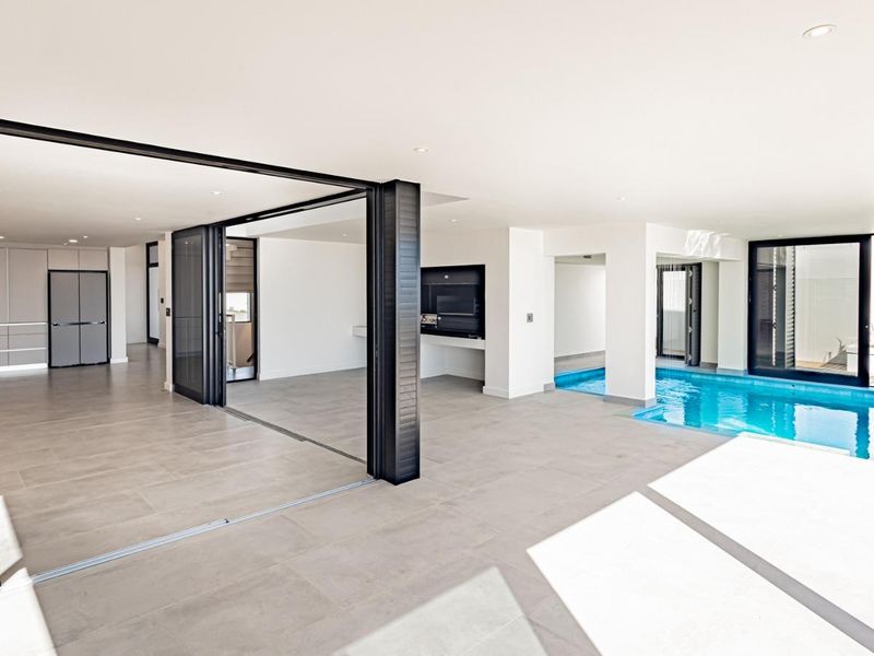 Spacious open-plan living area featuring a modern kitchen, seamless indoor-outdoor flow through sliding doors, and a unique integrated indoor swimming pool.