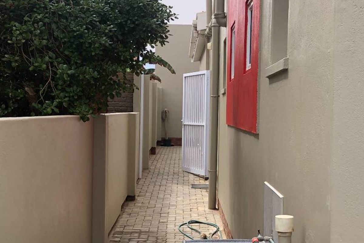 A side exterior walkway featuring paved flooring, a wall-mounted utility sink, and a gated entrance leading to the rear of the property.