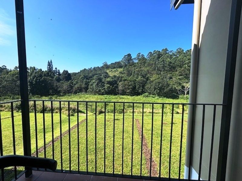 A private balcony featuring a metal balustrade and tiled flooring, offering scenic views of the surrounding green landscape and forest.