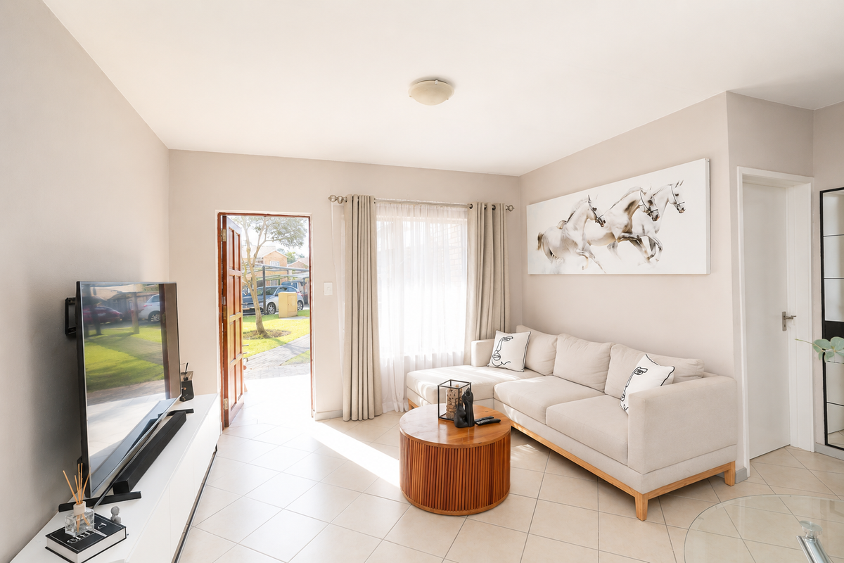 A bright and well-maintained living room featuring neutral tiled flooring, natural light from the entrance, and a clean, modern aesthetic.