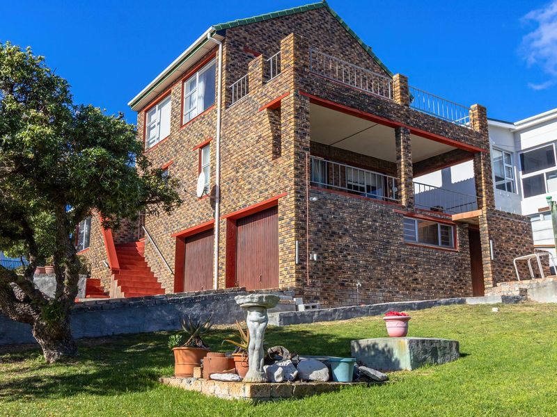 Rear view of a multi-level face brick house featuring a double garage, covered balcony, and an upper-level terrace with metal railings.