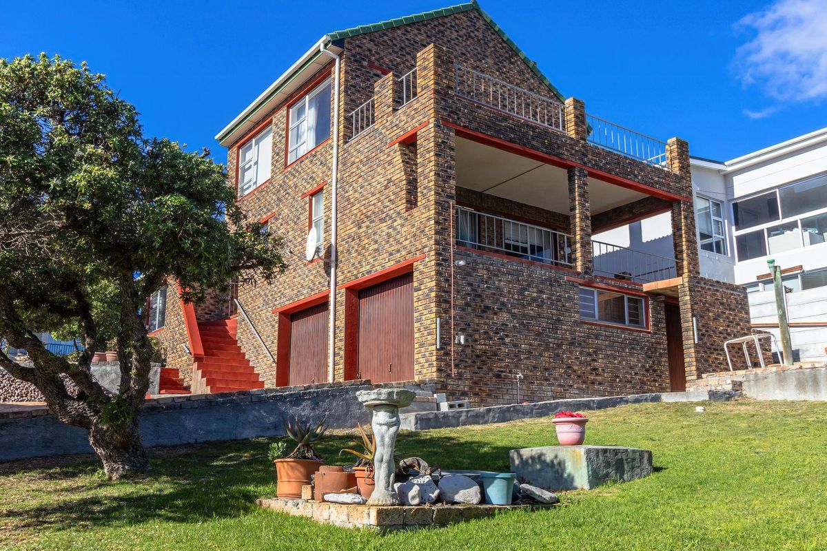 Rear view of a multi-level face brick house featuring a double garage, covered balcony, and an upper-level terrace with metal railings.