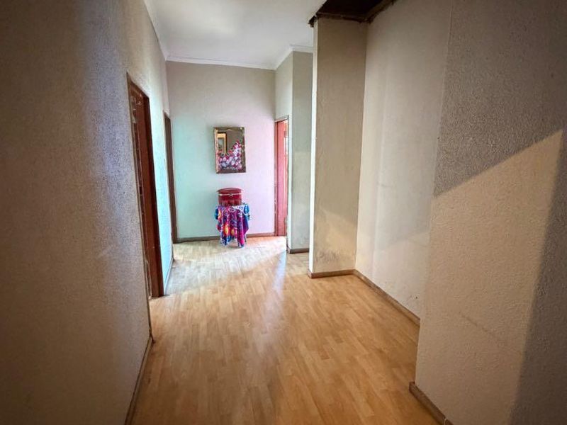A spacious hallway featuring laminate flooring and coving, currently requiring ceiling repairs and wall maintenance to restore its condition.
