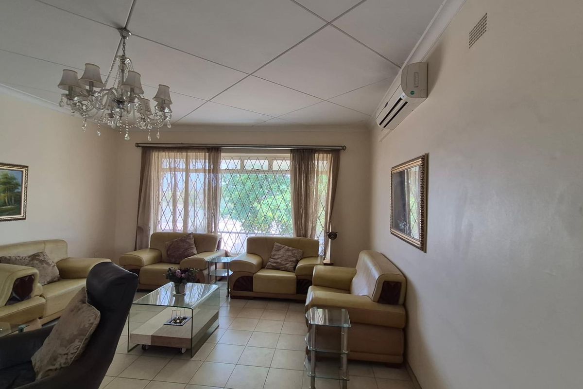 A living room featuring tiled flooring, a wall-mounted air conditioning unit, and a large window with security bars.