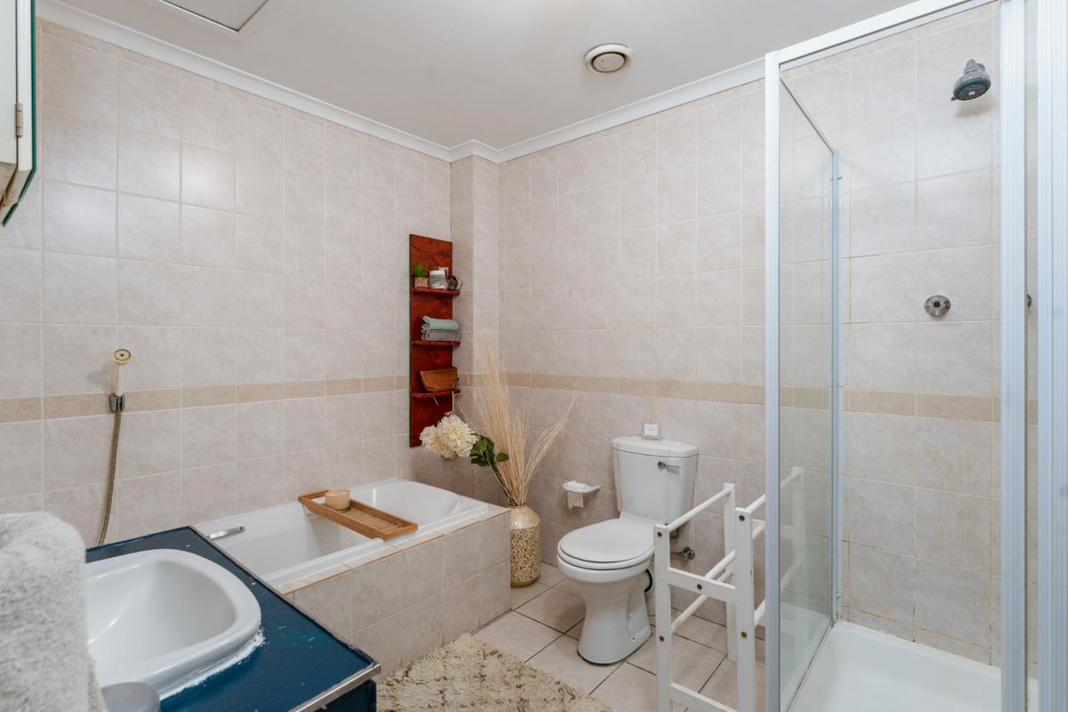 A functional bathroom featuring a built-in bathtub, separate shower enclosure, toilet, and vanity basin with neutral wall and floor tiling.