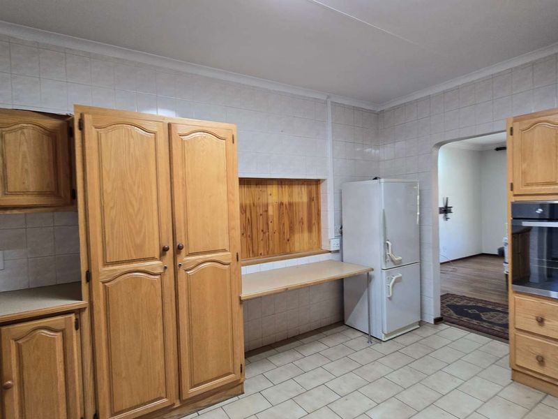 A functional kitchen featuring traditional wooden cabinetry, tiled wall finishes, and a built-in oven, offering a practical layout with a convenient pass-through window.