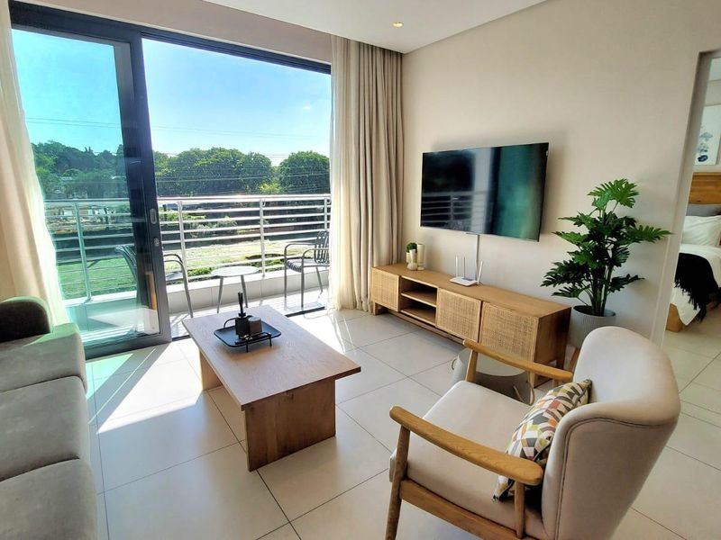 A bright living room featuring large sliding glass doors leading to a balcony, neutral tiled flooring, and recessed ceiling lighting.