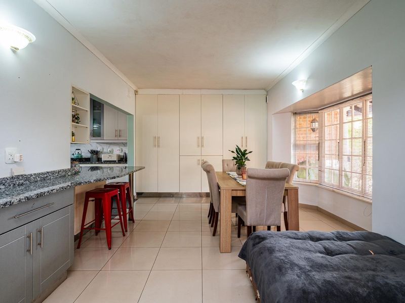Open-plan living and dining area featuring tiled flooring, a breakfast bar with granite countertops, built-in storage cabinetry, and a bright bay window.