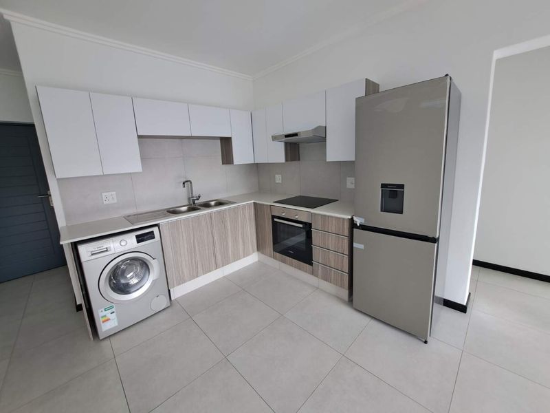 Modern kitchen featuring sleek cabinetry, stone countertops, integrated oven, hob, extractor fan, and tiled flooring in a clean, contemporary layout.