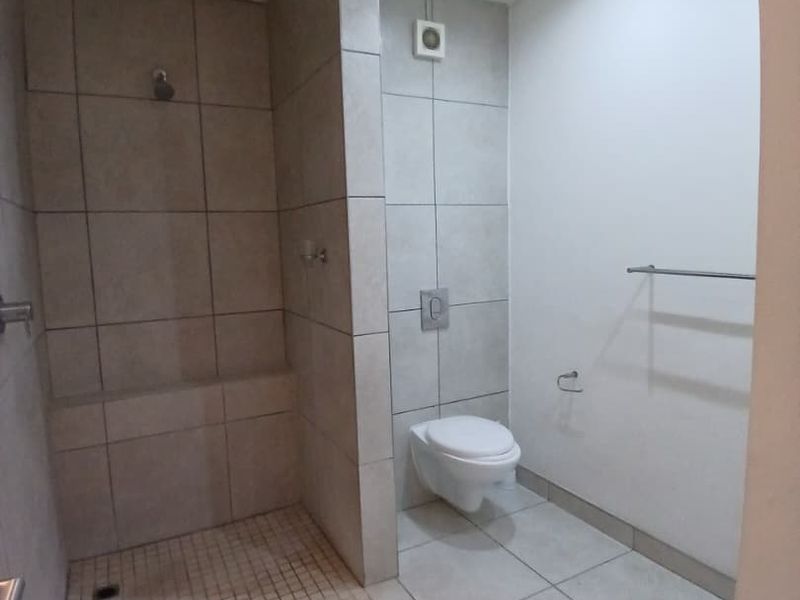 A modern, clean bathroom featuring a spacious walk-in shower with tiled finishes and a wall-mounted toilet.