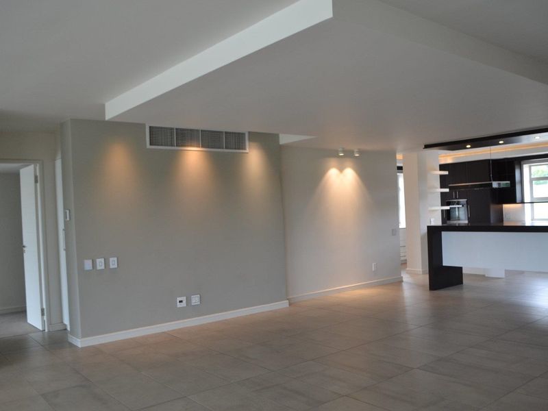 Spacious open-plan living area featuring neutral tiled flooring, recessed lighting, ducted air conditioning, and a modern kitchen with built-in cabinetry and breakfast bar.