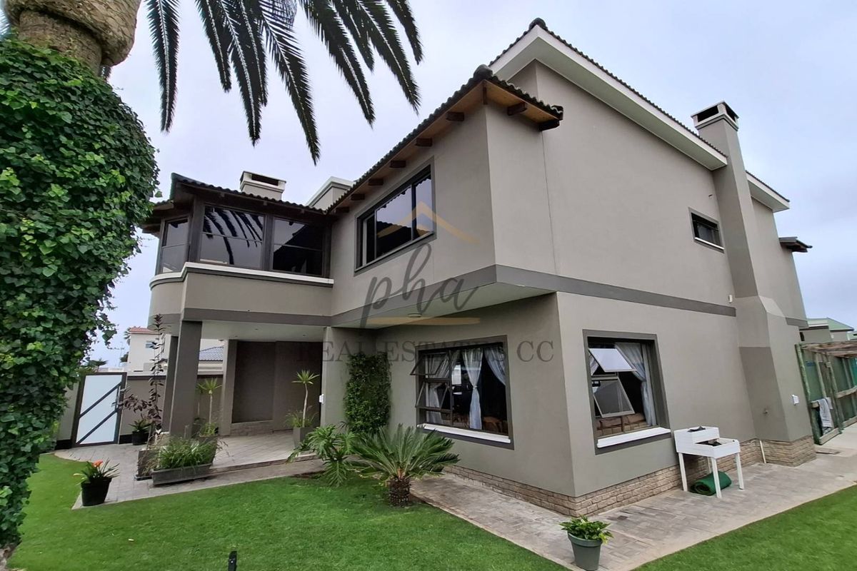 Rear view of a double-story house featuring a paved patio area, well-maintained lawn, and modern exterior finishes with aluminium window frames.