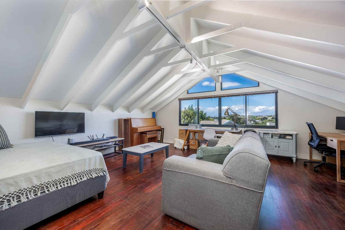 Spacious living area featuring a dramatic vaulted ceiling with exposed rafters, rich hardwood flooring, and large windows providing ample natural light and elevated views.