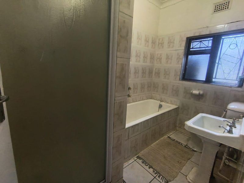 A dated bathroom featuring a bathtub, pedestal basin, and toilet with original wall and floor tiling, offering potential for a modern renovation.