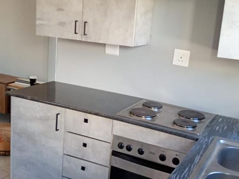 A functional kitchen featuring modern grey-toned cabinetry, stone countertops, a built-in electric oven and hob, and a stainless steel double sink.