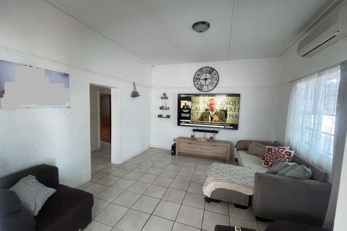 A functional living room featuring tiled flooring, a wall-mounted television, and a split-system air conditioning unit.