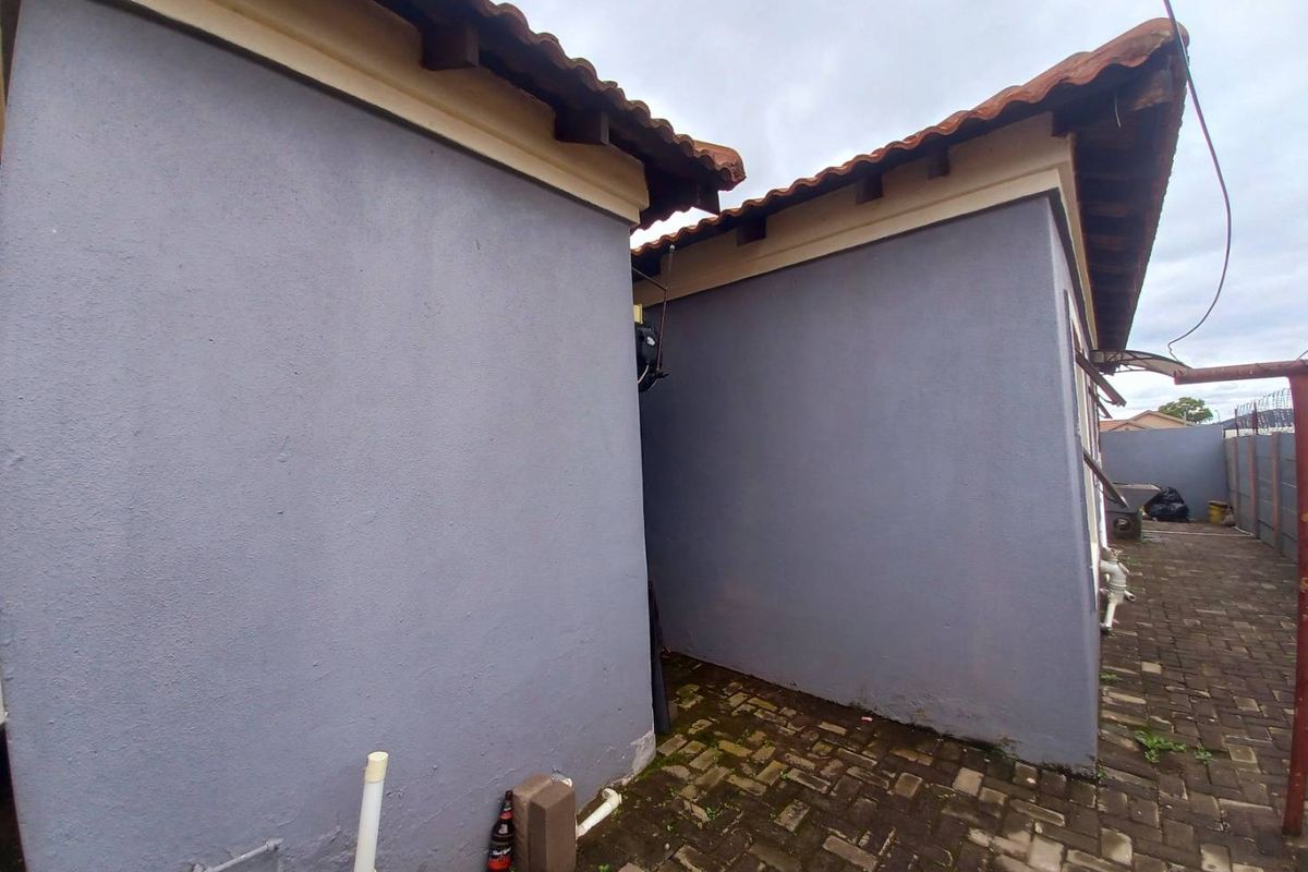 A view of the side exterior of the house featuring paved ground and painted masonry walls under a tiled roof.