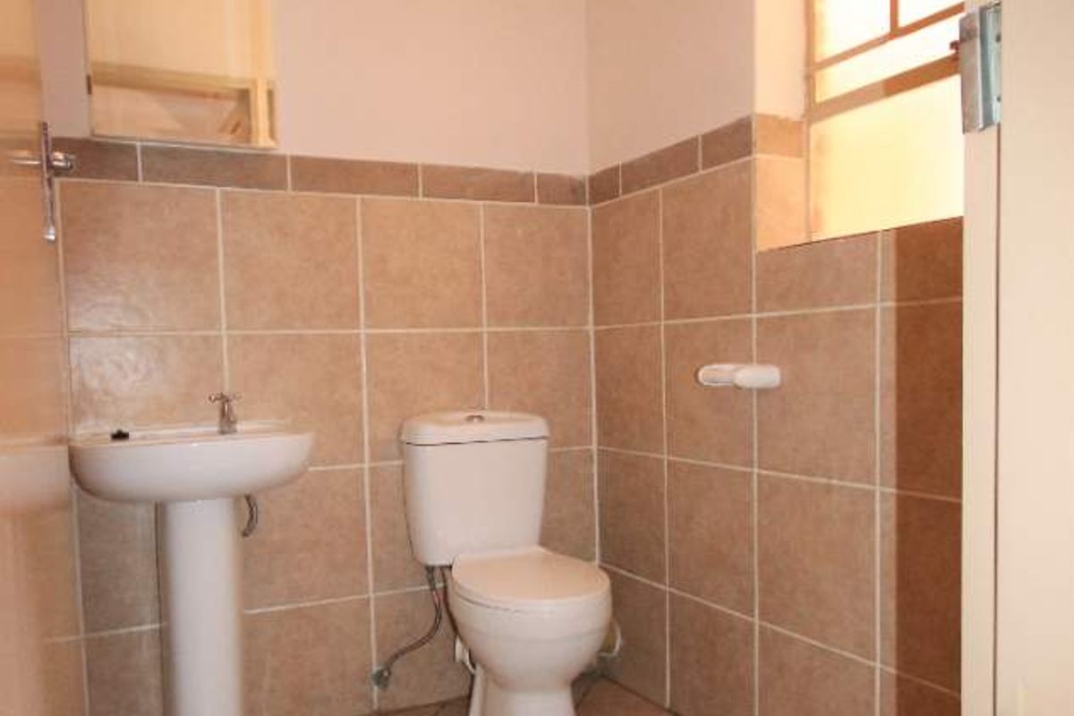 A functional bathroom featuring a pedestal basin, toilet, and neutral ceramic tiling throughout, offering a clean and practical space.