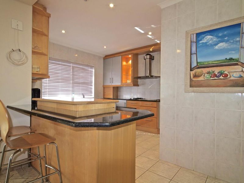 A functional kitchen featuring granite countertops, wooden cabinetry, tiled flooring, and integrated lighting, offering a practical layout for cooking and casual dining.