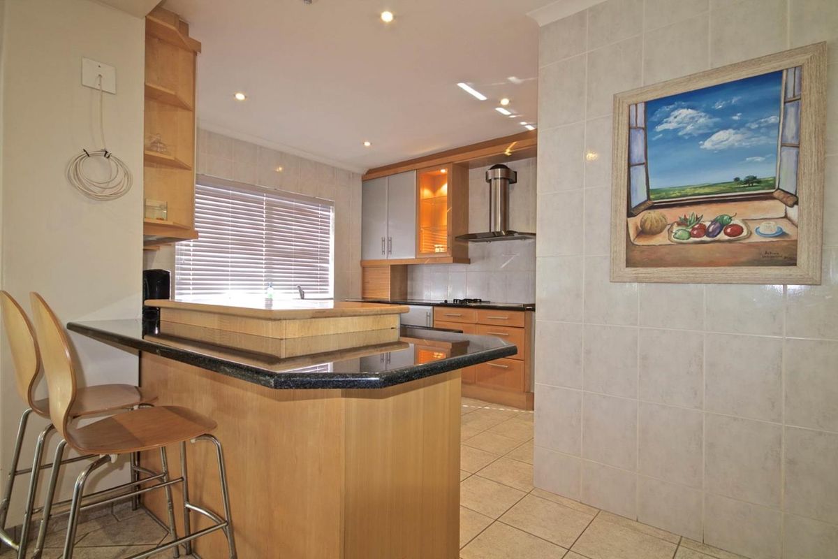 A functional kitchen featuring granite countertops, wooden cabinetry, tiled flooring, and integrated lighting, offering a practical layout for cooking and casual dining.