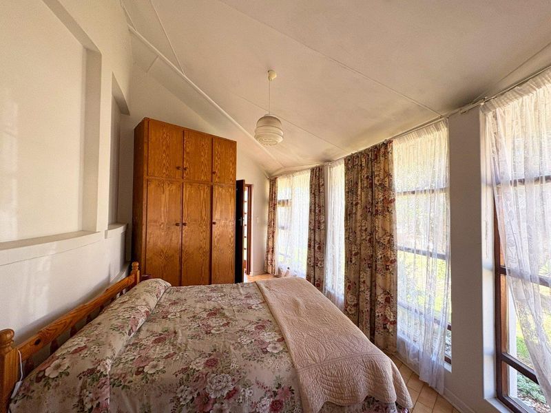 A bedroom featuring a sloped ceiling, built-in wooden wardrobe, and large windows that provide ample natural light.
