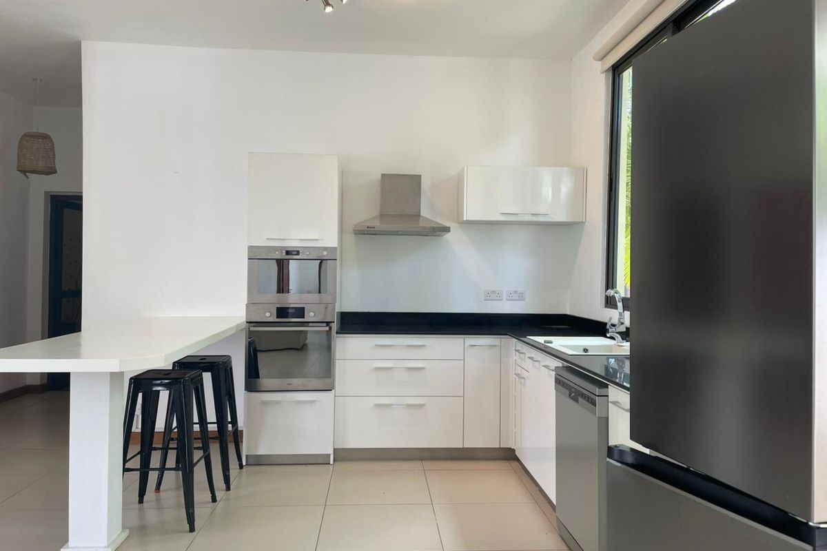 Modern kitchen featuring white cabinetry, black countertops, built-in oven, microwave, extractor fan, and integrated dishwasher with a breakfast bar extension.