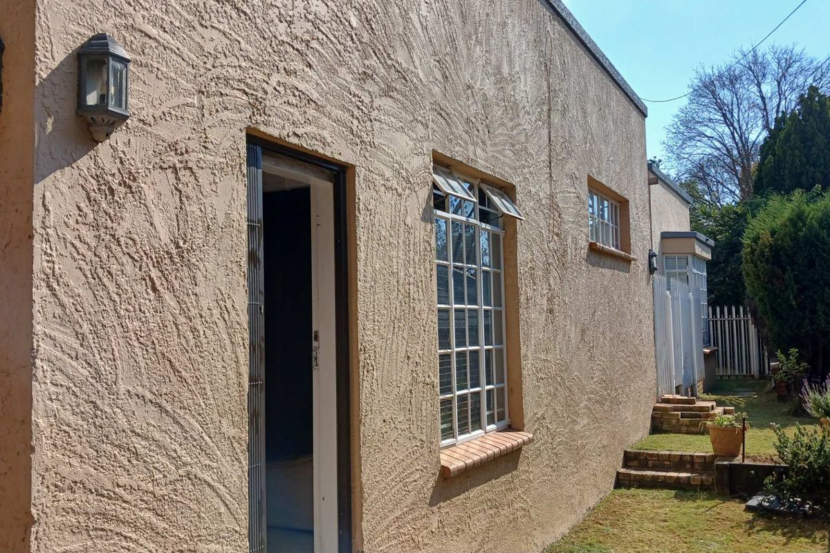 Rear exterior view of the cottage featuring textured stucco walls, multi-pane windows, and brick garden steps leading to the backyard.