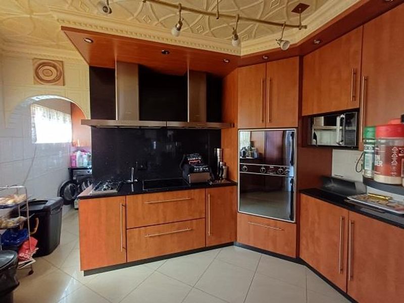 A functional kitchen featuring wood-finish cabinetry, integrated oven, extractor fan, and tiled flooring, with an adjacent scullery area visible through the archway.