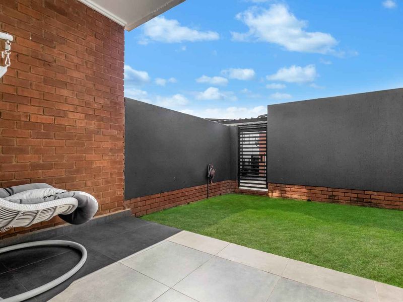 A private outdoor patio area featuring tiled flooring, a brick feature wall, and a small enclosed garden space with a secure metal gate.