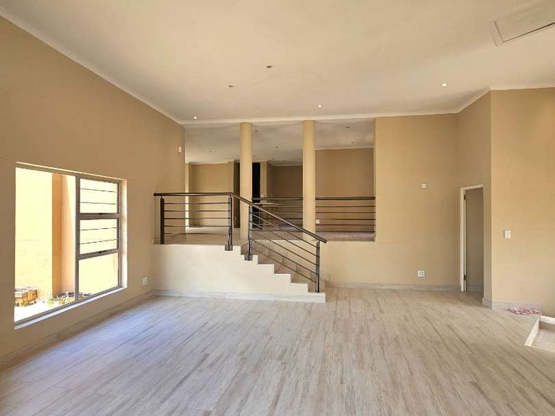 Spacious open-plan living area featuring modern tiled flooring, recessed lighting, and a central staircase with a metal balustrade leading to an upper level.