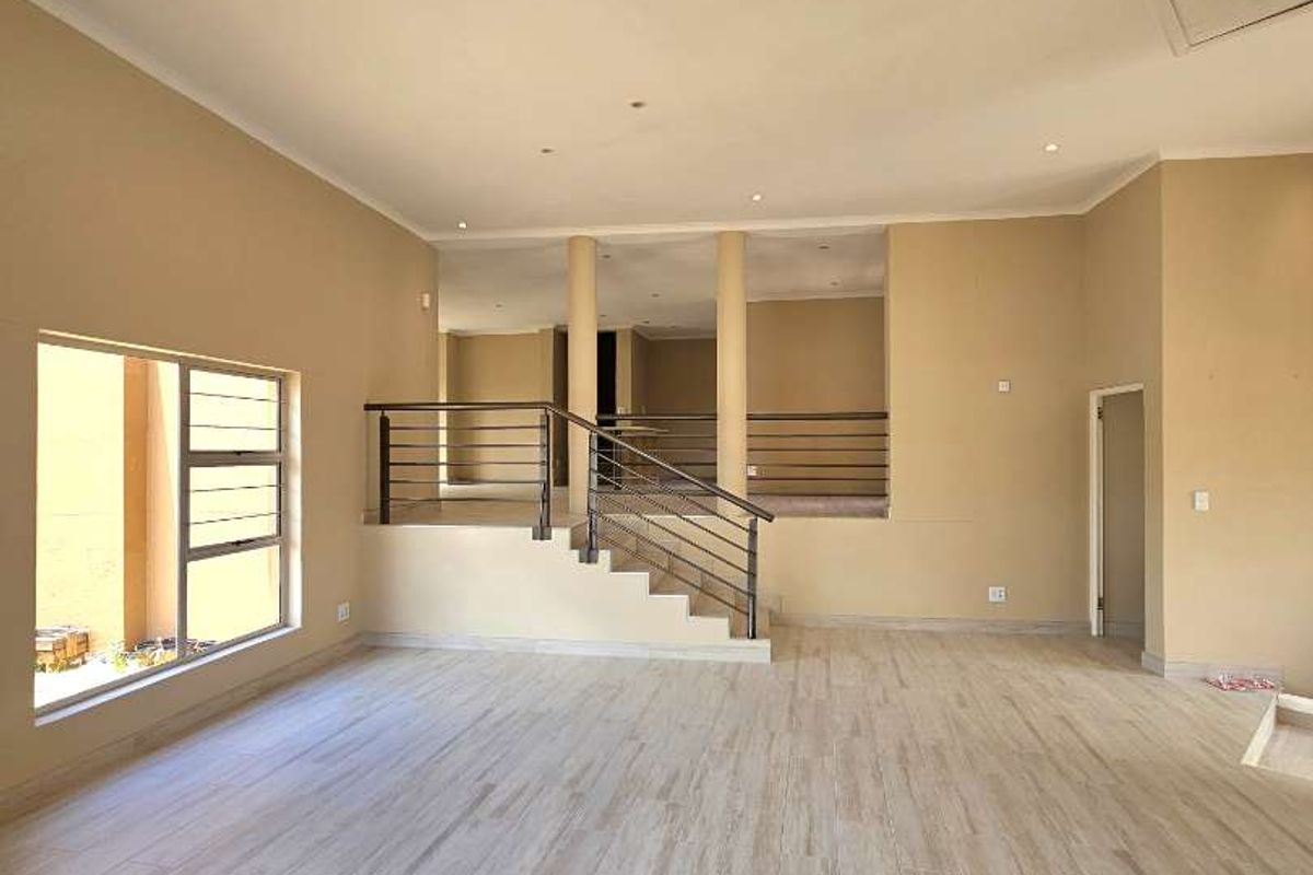 Spacious open-plan living area featuring modern tiled flooring, recessed lighting, and a central staircase with a metal balustrade leading to an upper level.
